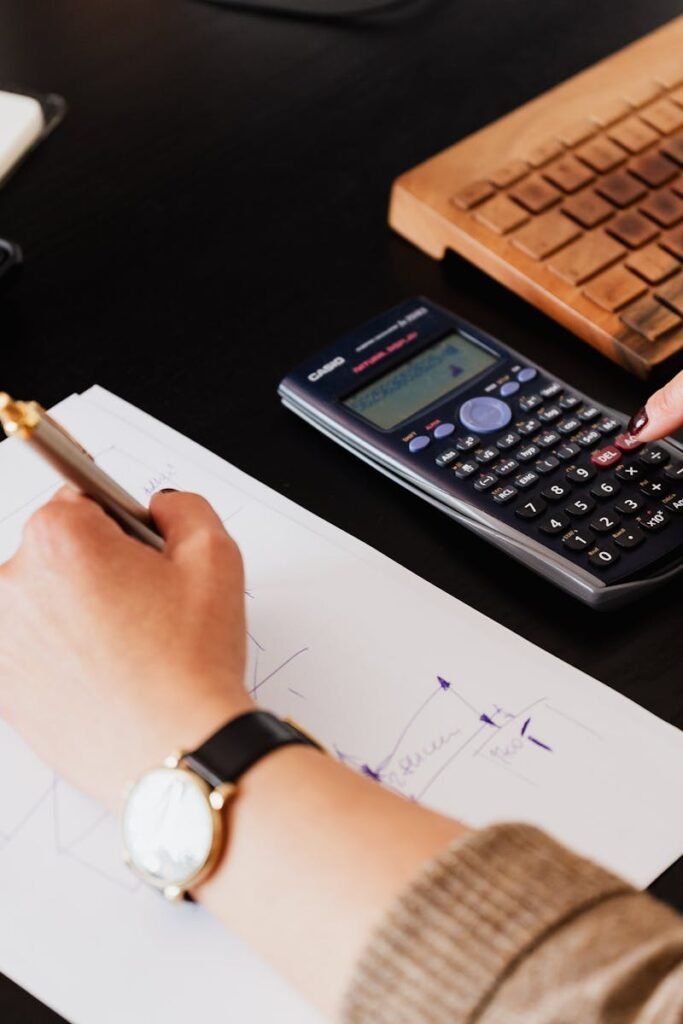 Close-up of hands working with a calculator and notebook on a desk, analyzing documents.